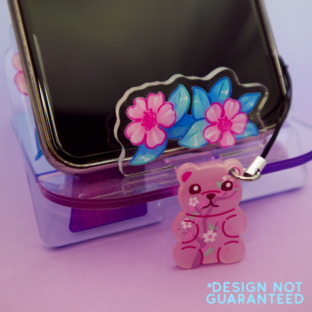 Phone on a floral stand, with a pink sakura gummy bear-shaped phone charm attached.