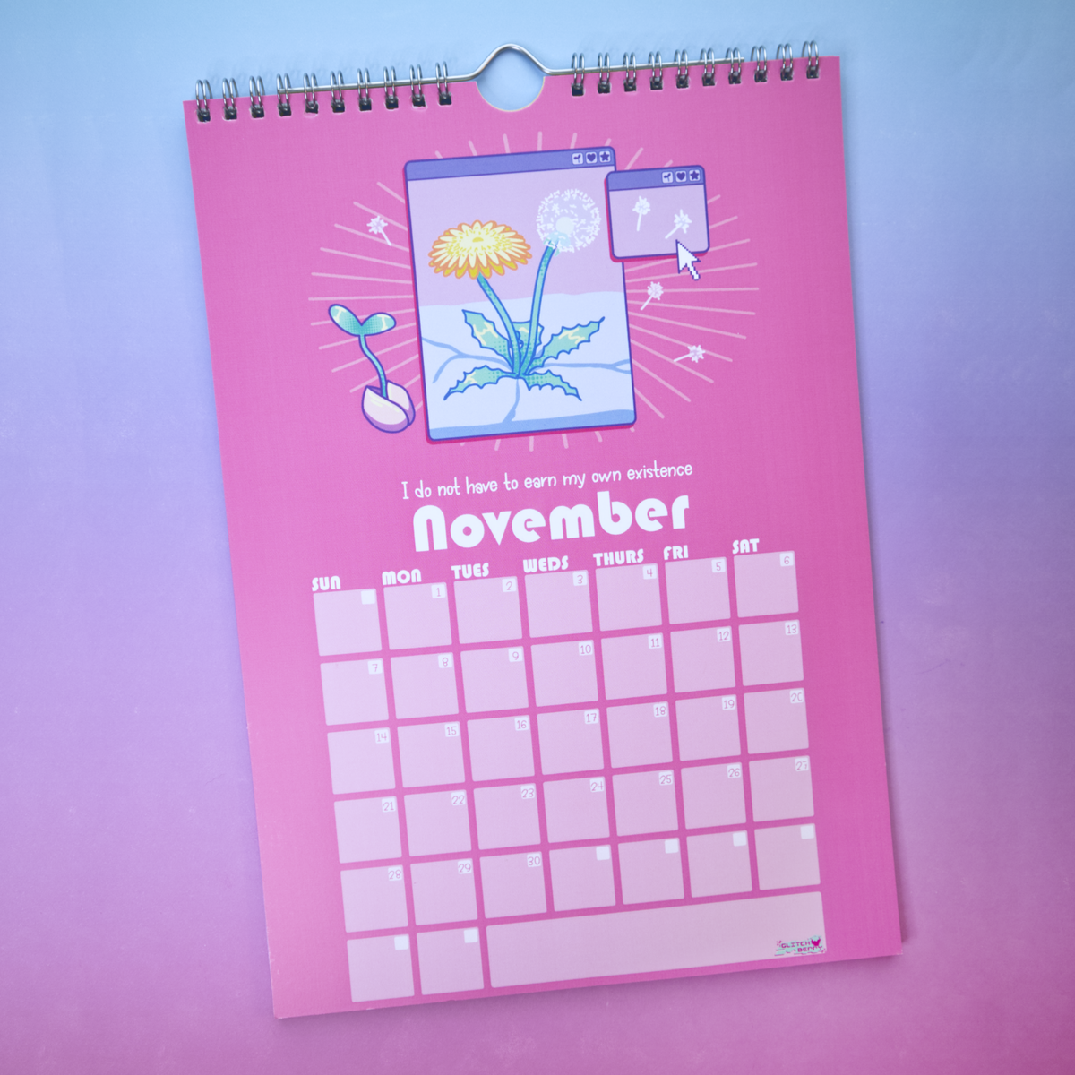 A spiral-bound 2027 wall calendar open to November's page, featuring an illustration of a dandelion sprouting from concrete, and blank grid boxes for daily planning.