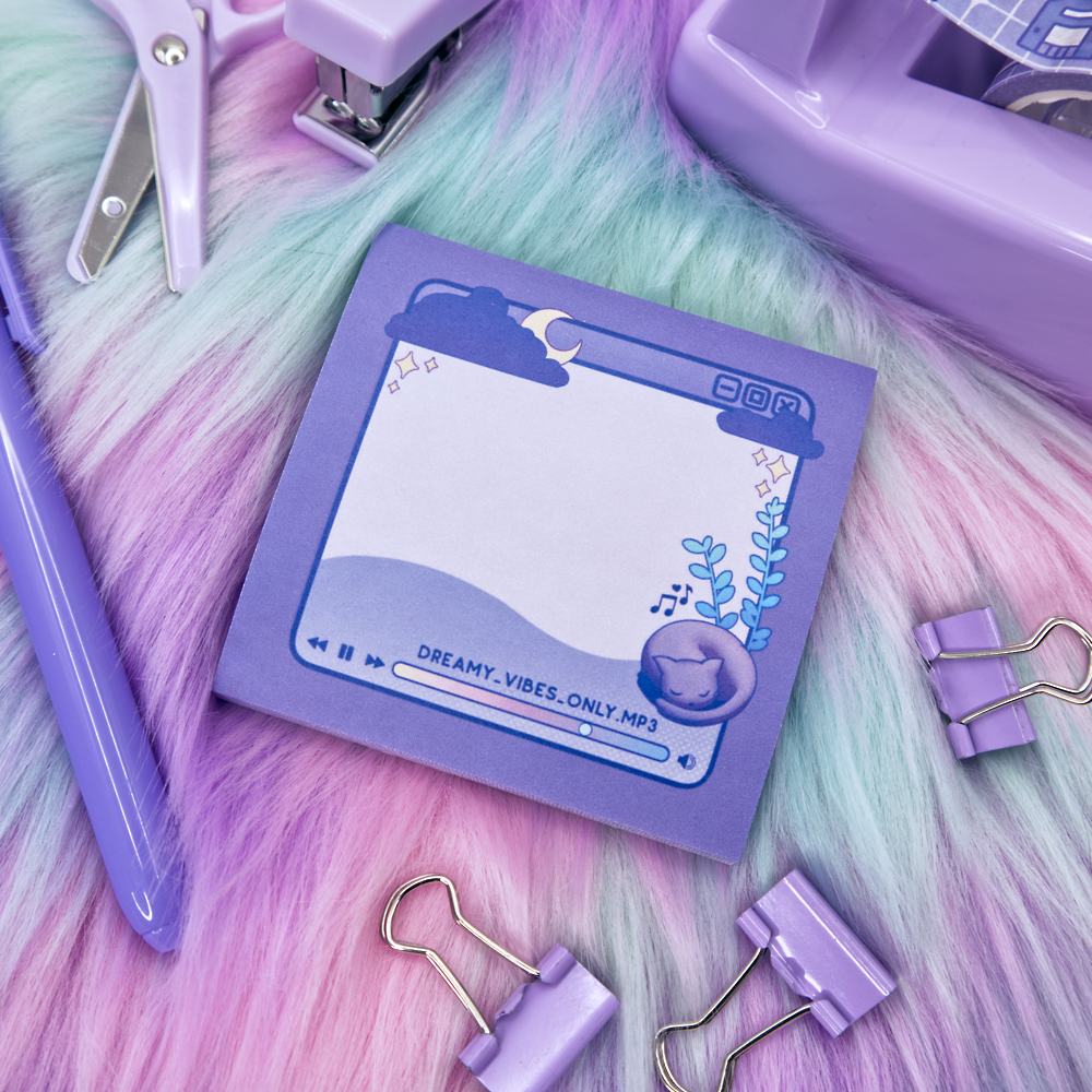 Purple sticky note pad with music player design featuring a cat and a plant on a fluffy pink and green surface surrounded by stationery items
