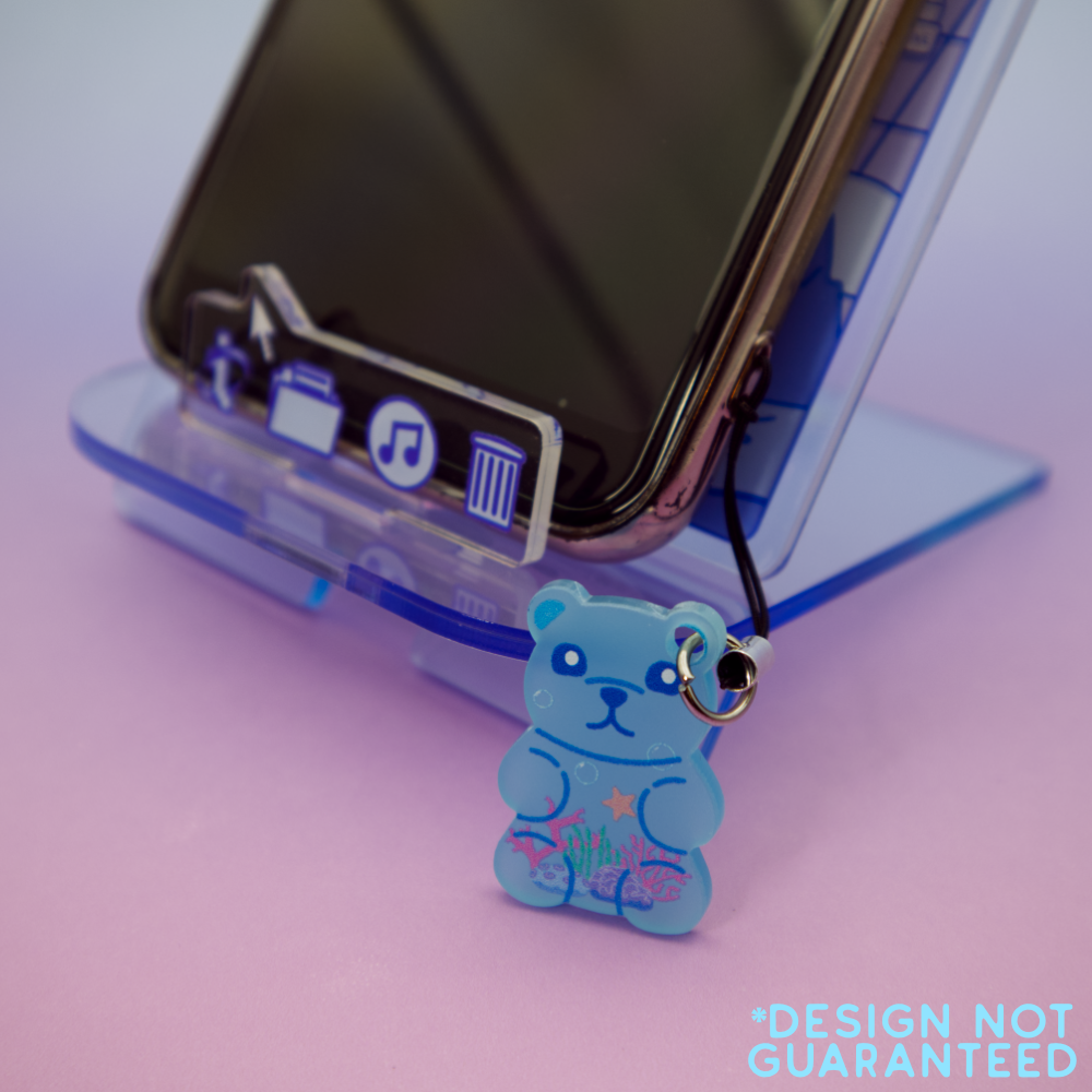 Blue water-themed bear-shaped phone charm on a pink surface with a phone and stand in the background.
