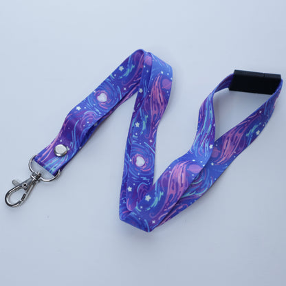 A purple space-patterned lanyard with a breakaway safety buckle and silver lobster clasp sits on a white background. 