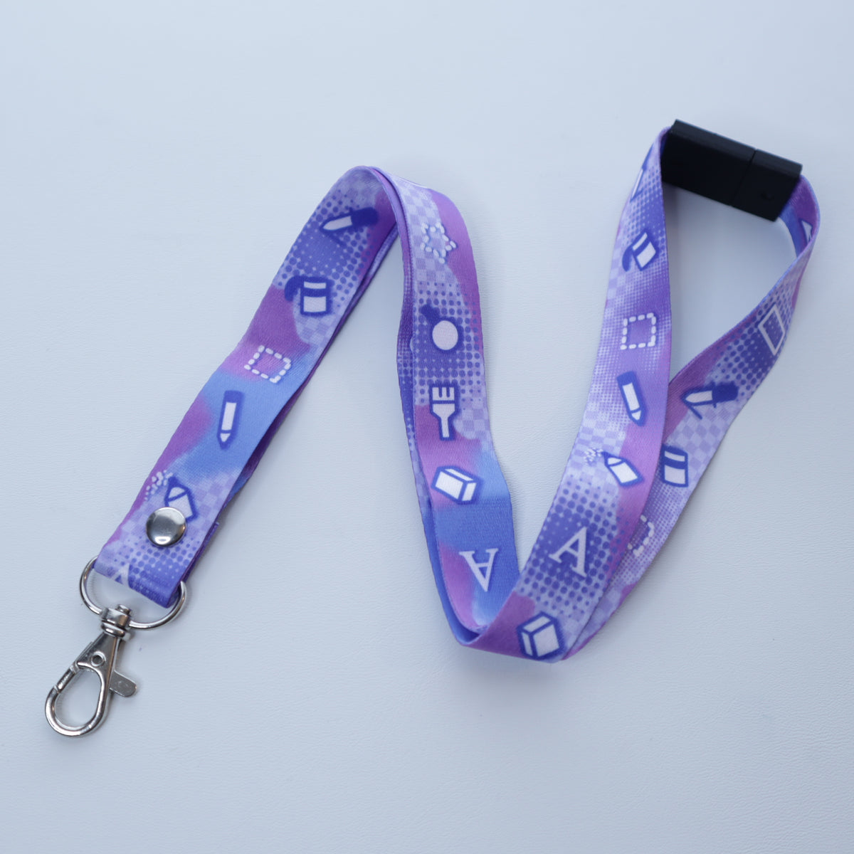 A pastel purple digital art tool patterned lanyard with a breakaway safety buckle and silver lobster clasp sits on a white background. 