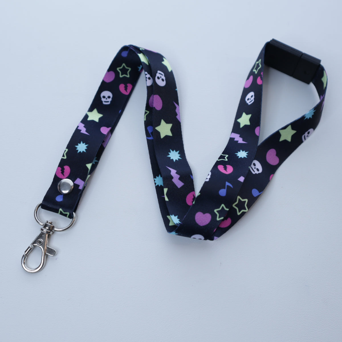 A black, early 2000's "scene kid" patterned lanyard with a breakaway safety buckle and silver lobster clasp sits on a white background. 