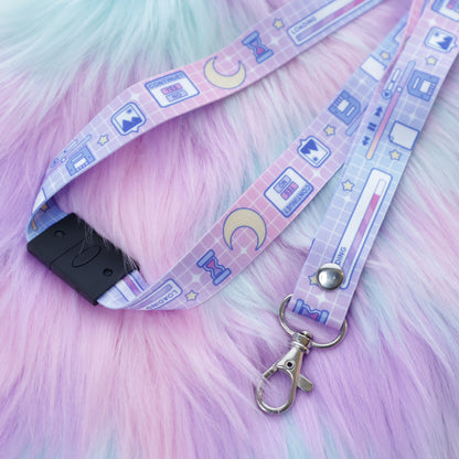 A pastel pink and blue computer UI patterned lanyard with a breakaway safety buckle and silver lobster clasp sits on a fuzzy teal and pink background. 