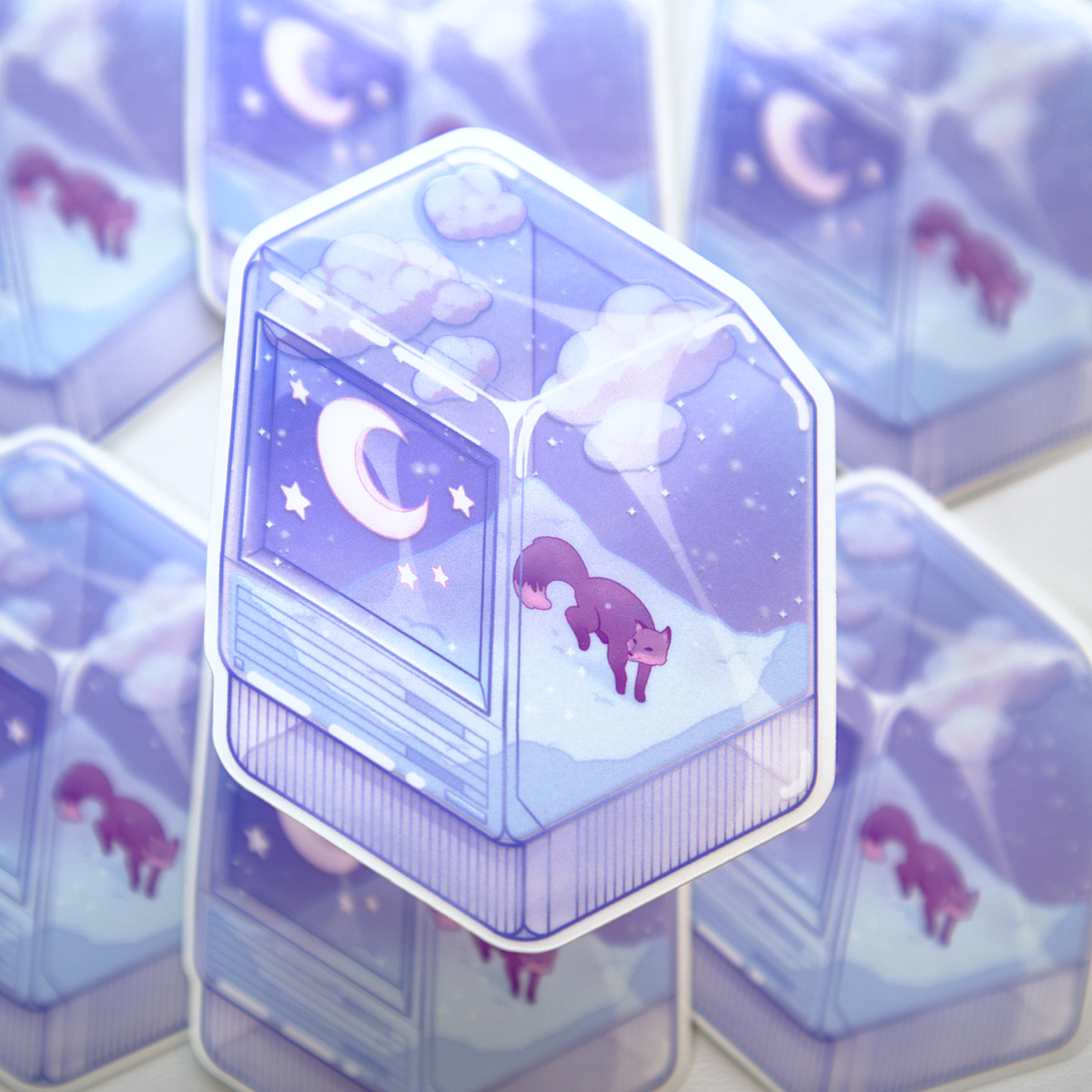 A die-cut sticker featuring a winter scene with a small fox, night sky, and snow, inside of a translucent PC tower like a snow globe.  Sticker is photographed on a background of a stack of the same sticker.