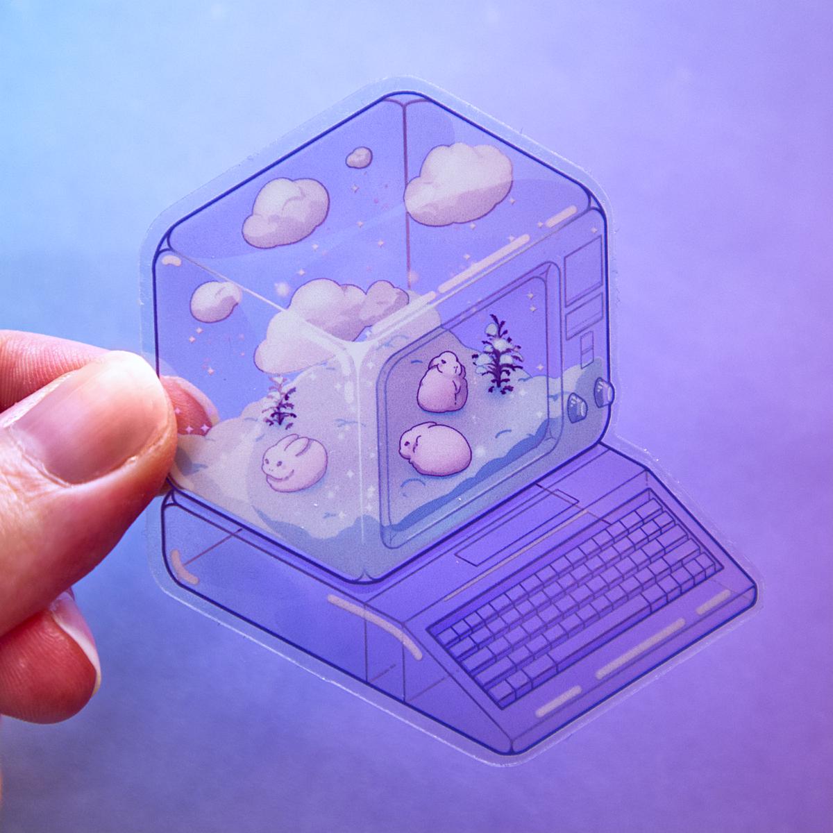 A hand holds a die-cut sticker featuring a winter scene with small rabbits, bare shrubs, and snow, inside of a translucent PC tower like a snow globe.  Sticker is photographed on a purple background.