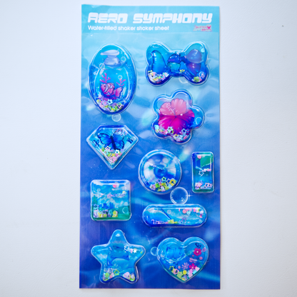 A sheet of clear plastic stickers filled with water and glitter confetti, featuring various Frutiger Aero themed illustrations including fish, butterflies, and flowers.  It is displayed on its blue underwater-patterned backing card, with text at the top that says "Aero Symphony: Water-filled shaker sticker sheet by GlitchBerry"