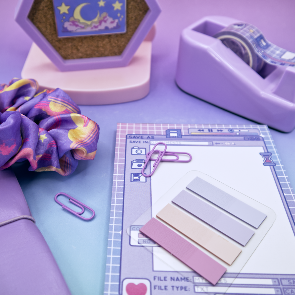 Stationery items including a purple scrunchie, tape dispenser, and paper clips on a purple surface.